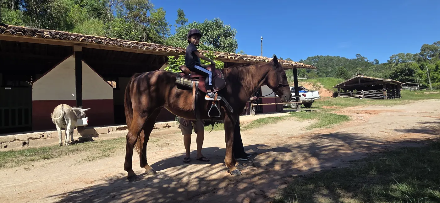 Criança a cavalo em frente às baias da fazenda